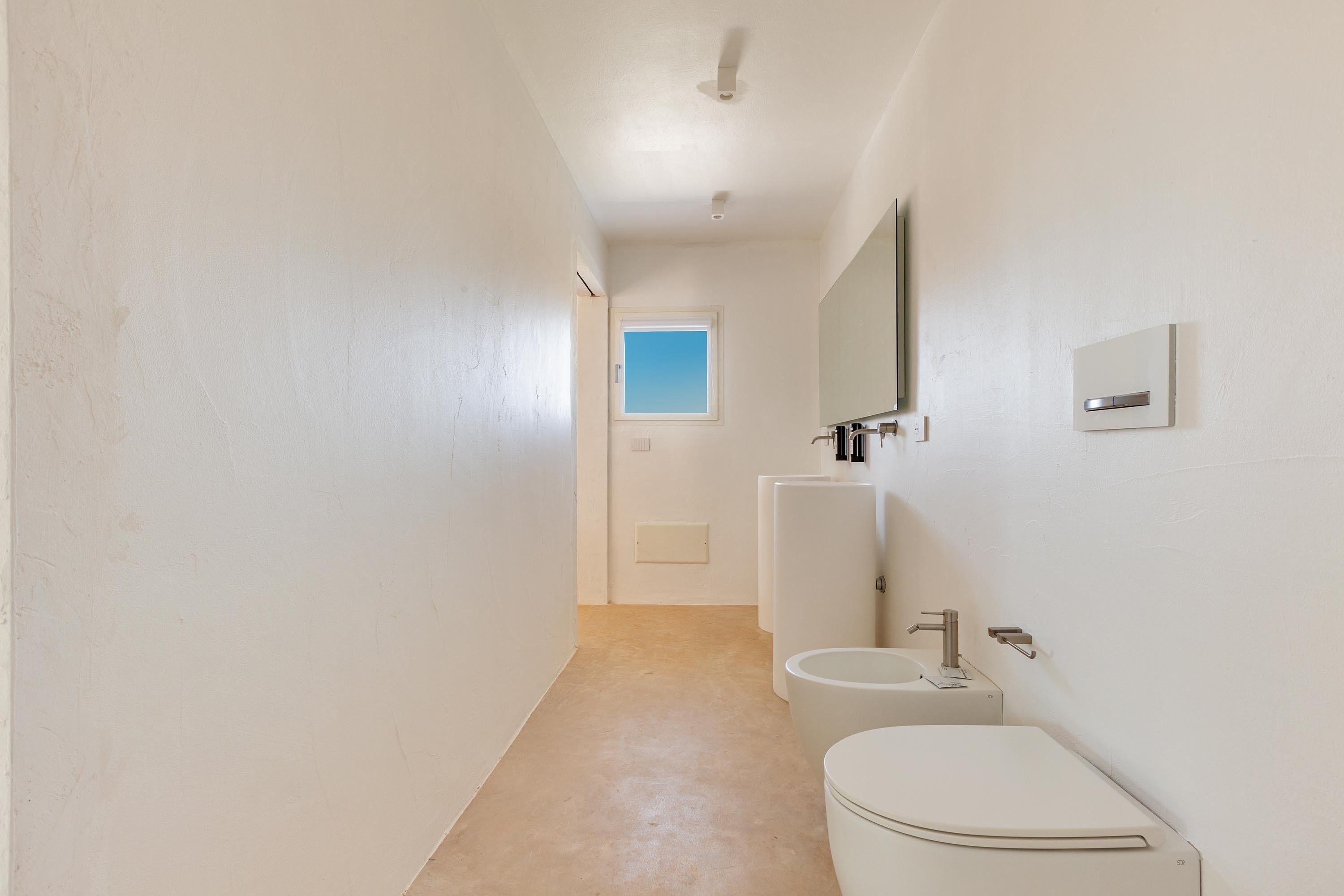 A narrow hallway leading to a bathroom with a toilet, sink, and mirror.