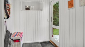 A room with white paneled walls, a door with a glass panel, a small table with a colorful tablecloth, and a wicker chair. - Amazing home in Idestrup with kitchen (Idestrup)
