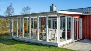A glass-enclosed patio with wicker furniture and a red building in the background. - Amazing home in Idestrup with kitchen (Idestrup)
