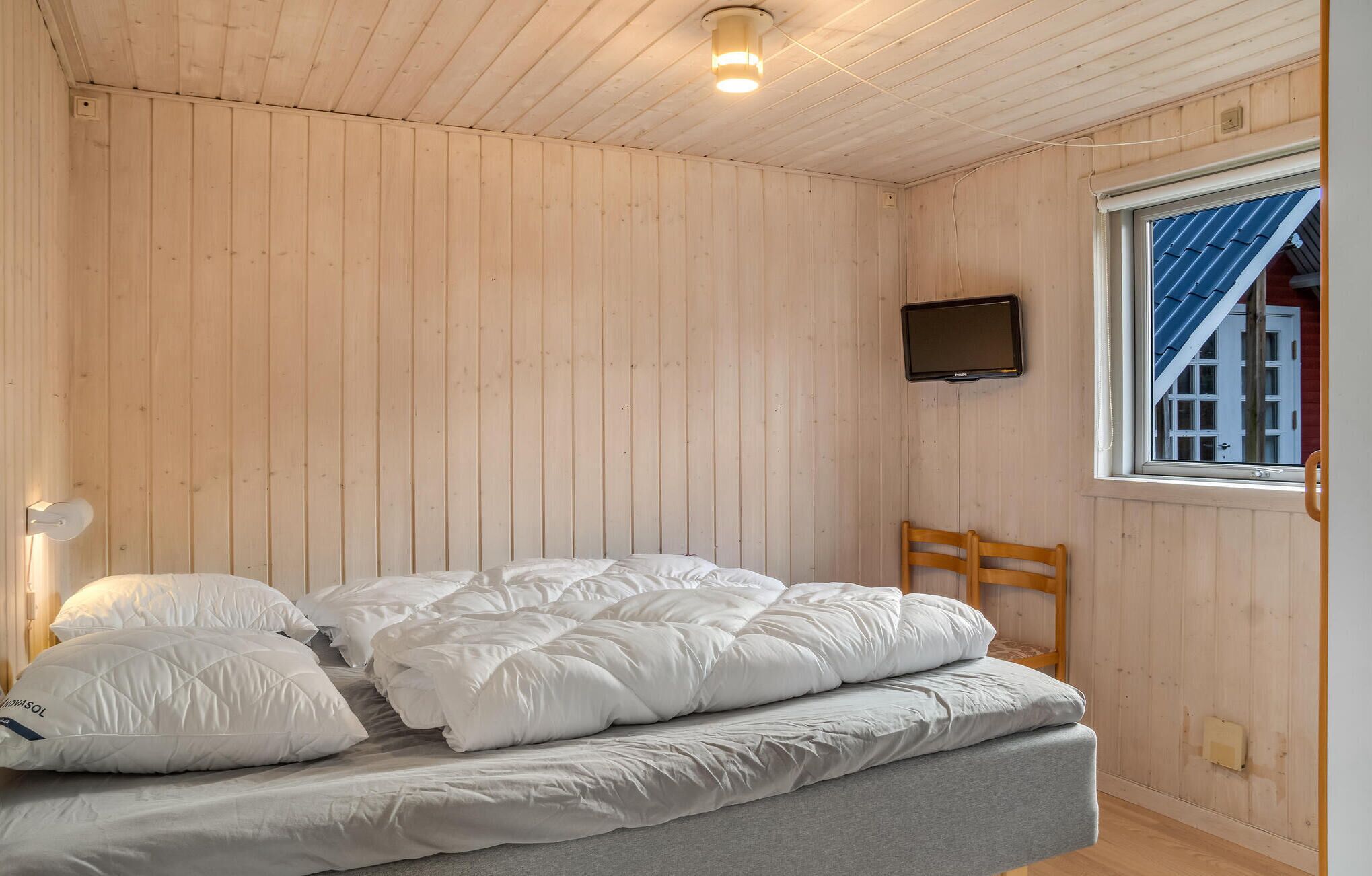 Un lit simple avec une literie blanche, dans une pièce aux murs en bois et au plafond en pente.