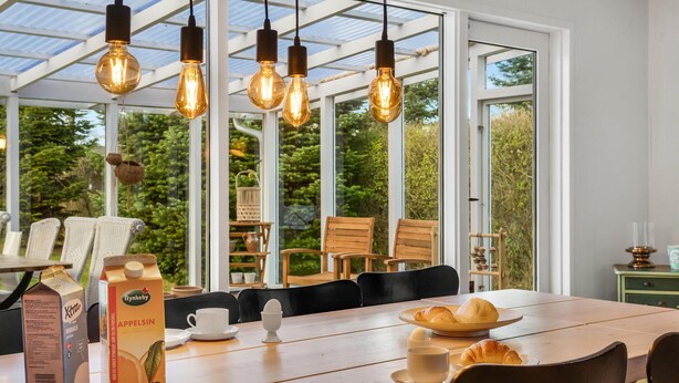 A dining area with a wooden table, chairs, and a view of greenery through large windows. - Amazing home in Idestrup with kitchen (Idestrup)