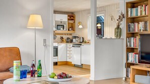 A modern living room with a sofa, a coffee table with drinks and a book, a kitchen area with appliances, and a bookshelf with books and a TV. - Amazing home in Idestrup with kitchen (Idestrup)