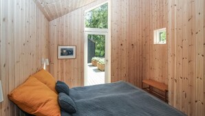 A bedroom with a bed, a bench, and a door leading to an outdoor area with plants. - 2 bedroom cozy home in Samsø (Samsø)