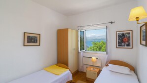 Une chambre avec deux lits simples, une armoire, une table de chevet avec une lampe et une fenêtre donnant sur un paysage.