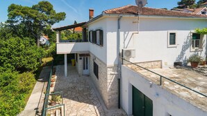Une maison à deux étages avec une cour pavée de pierres, un balcon et une antenne parabolique.