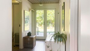 Een gang met houten vloer, een radiator, een potplant en een schuifdeur van glas die uitkomt op een groenrijke buitenruimte.