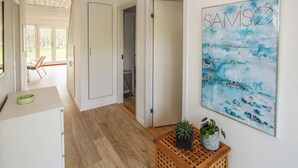 Een gang met een houten vloer, een witte deur en een schilderij van een kustlandschap.