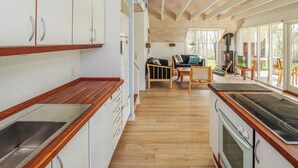 Een moderne keuken met houten aanrechtbladen en witte kastjes, een zithoek met een bank en stoelen, en grote ramen die zorgen voor natuurlijk licht.