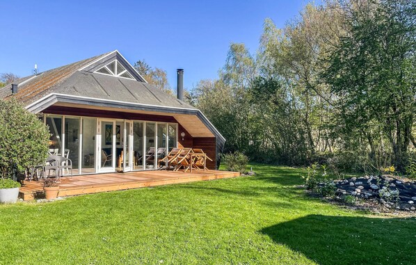 Una casa moderna con un amplio ventanal, una terraza de madera y un jardín césped.