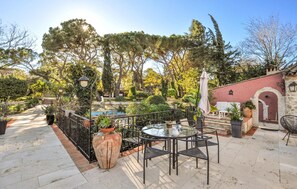 Relax in a serene patio surrounded by lush greenery and mature trees, featuring a seating area with a table and chairs.