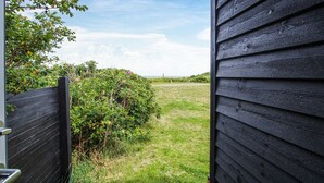 Blick durch ein Holztor auf eine Wiese mit Zaun und Büschen.