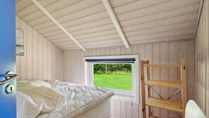 Un dormitori amb un llit, una finestra amb vista a un camp verd i una escala de fusta.