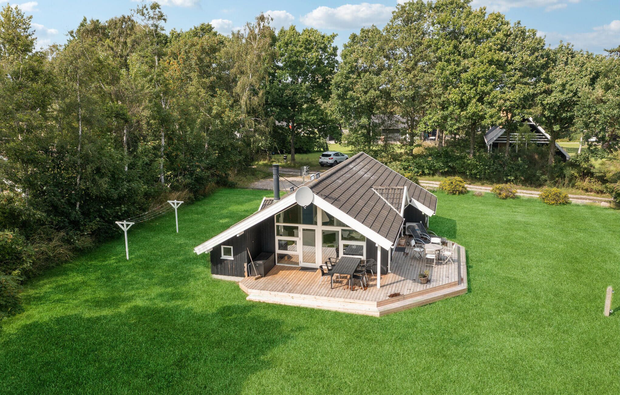 Une maison de plain-pied dotée d’une terrasse, entourée d’une pelouse bien entretenue et d’arbres touffus.