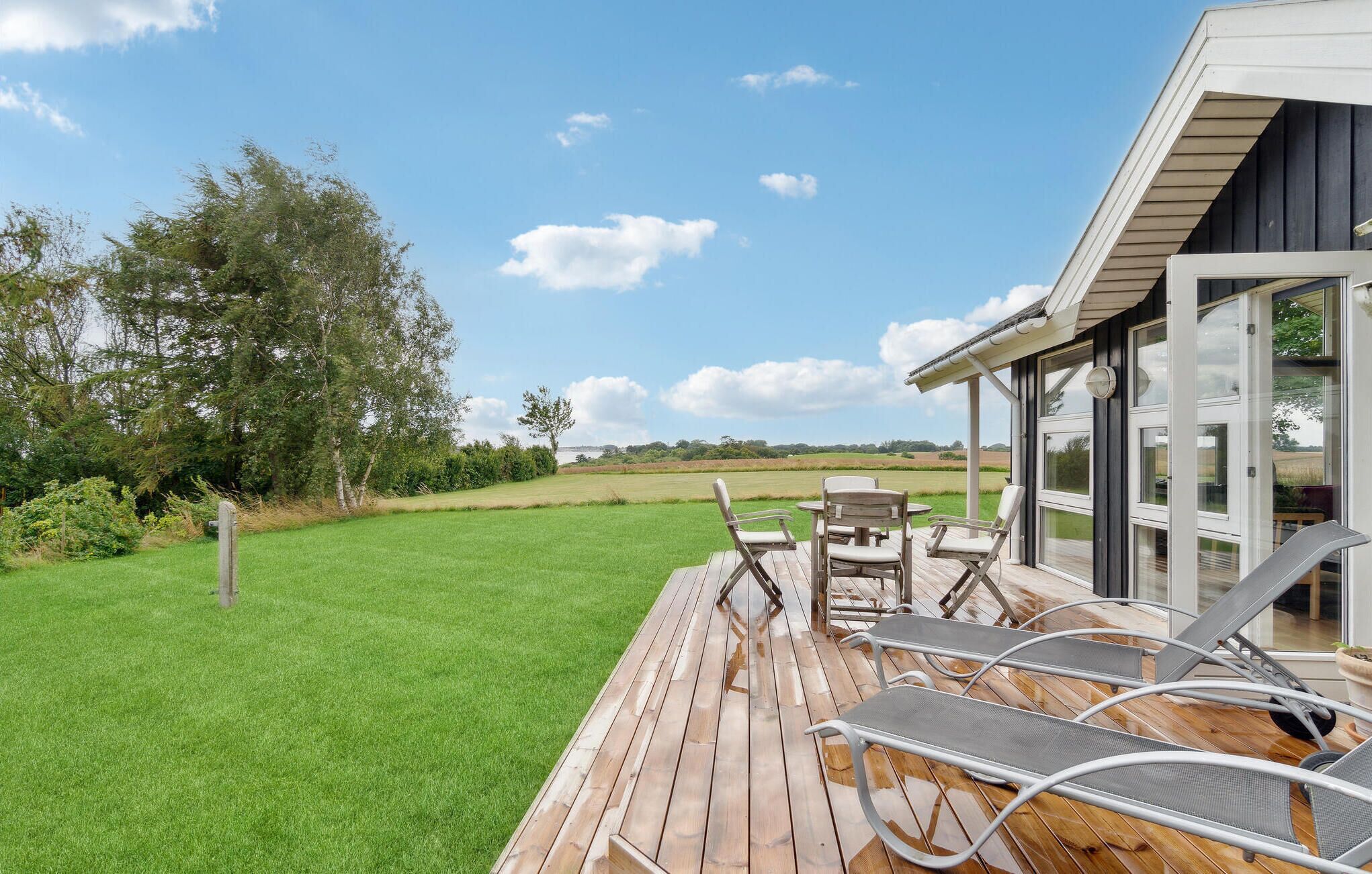 A wooden deck with outdoor furniture overlooking a grassy field and trees.