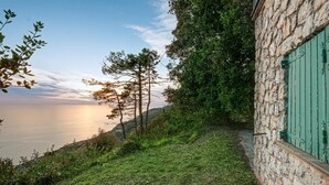 A stone building with a green shutter, a grassy path, and a view of the sea at sunset. - Awesome home in La Spezia with WiFi (La Spezia)