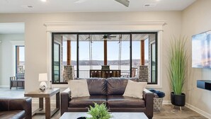 A living room with a brown leather sofa, a coffee table with a plant, and a view of a body of water through large windows.