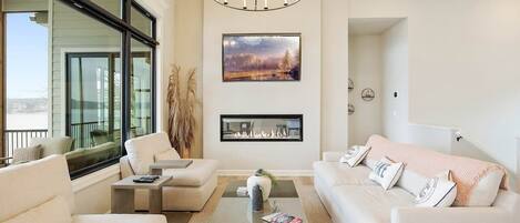 A modern living room with a fireplace, large windows, and a chandelier.
