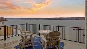 A balcony with a view of a lake, a fire pit, and two Adirondack chairs.