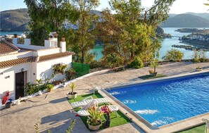 A pool area with a view of a lake and hills, surrounded by trees and a white building with a tiled roof. - Stunning home in Iznajar (Iznajar)