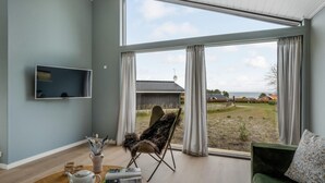 Een moderne woonkamer met een groot raam, een flatscreen-tv, een groene bank en een fauteuil met een bont plaid.