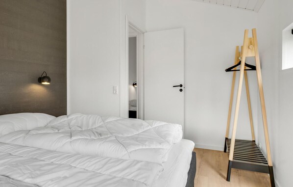 Ein Schlafzimmer mit einem Bett, einem hölzernen Kleiderständer und einer Wandleuchte.