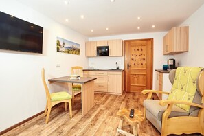 A compact living space with a kitchenette, a dining area, and a seating area with a TV and a remote control on a small table.