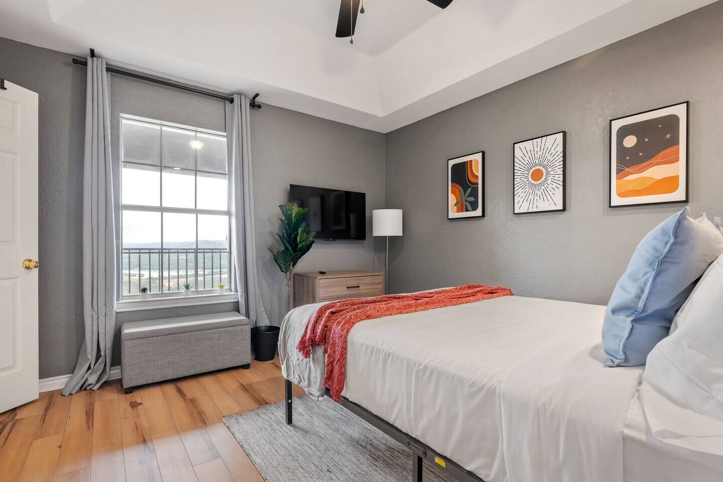 Une chambre à coucher avec un lit, une télévision, une fenêtre avec des rideaux et des œuvres d’art accrochées au mur.