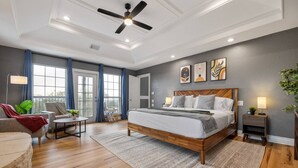A modern bedroom with a large bed, a ceiling fan, and a view of the outdoors through a sliding door. - Pet-Friendly! Pool/Spa, Views, Arcade, EV Charger (Wimberley)