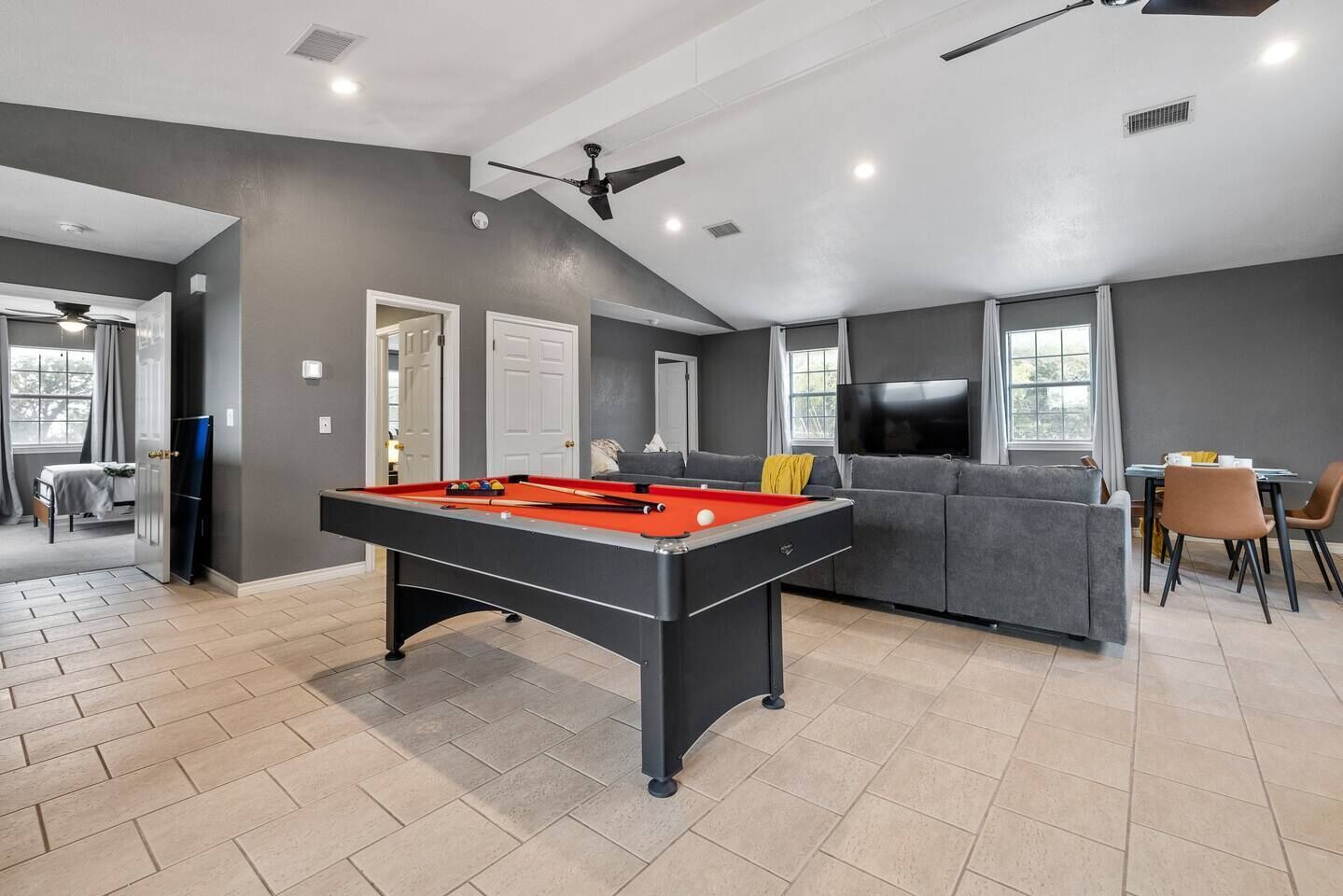Un salon moderne avec une table de billard, des canapés gris, un téléviseur et un coin repas.