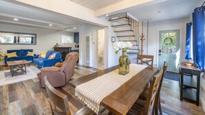 Amplia sala de estar con una mesa de comedor de madera, sofás azules y una escalera que conduce a un nivel superior.