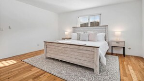 Ein Schlafzimmer mit einem hölzernen Bett, weißer Bettwäsche, einem gemusterten Teppich und zwei Nachttischlampen.