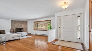 Ein geräumiges Wohnzimmer mit Kamin aus Stein, einem weißen Sofa und einem großen Fenster mit Jalousien.