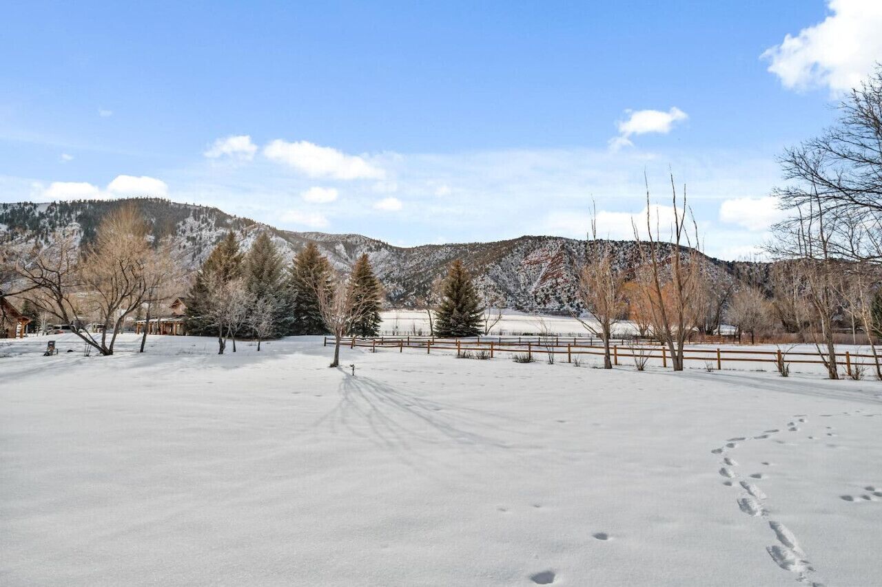 A snow-covered landscape with a wooden fence, trees, and a mountain in the background.