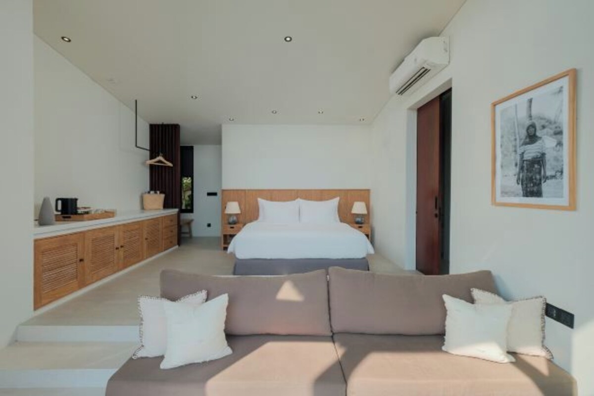 A modern hotel room with a large bed, a sofa, a wooden cabinet, and a framed picture on the wall.