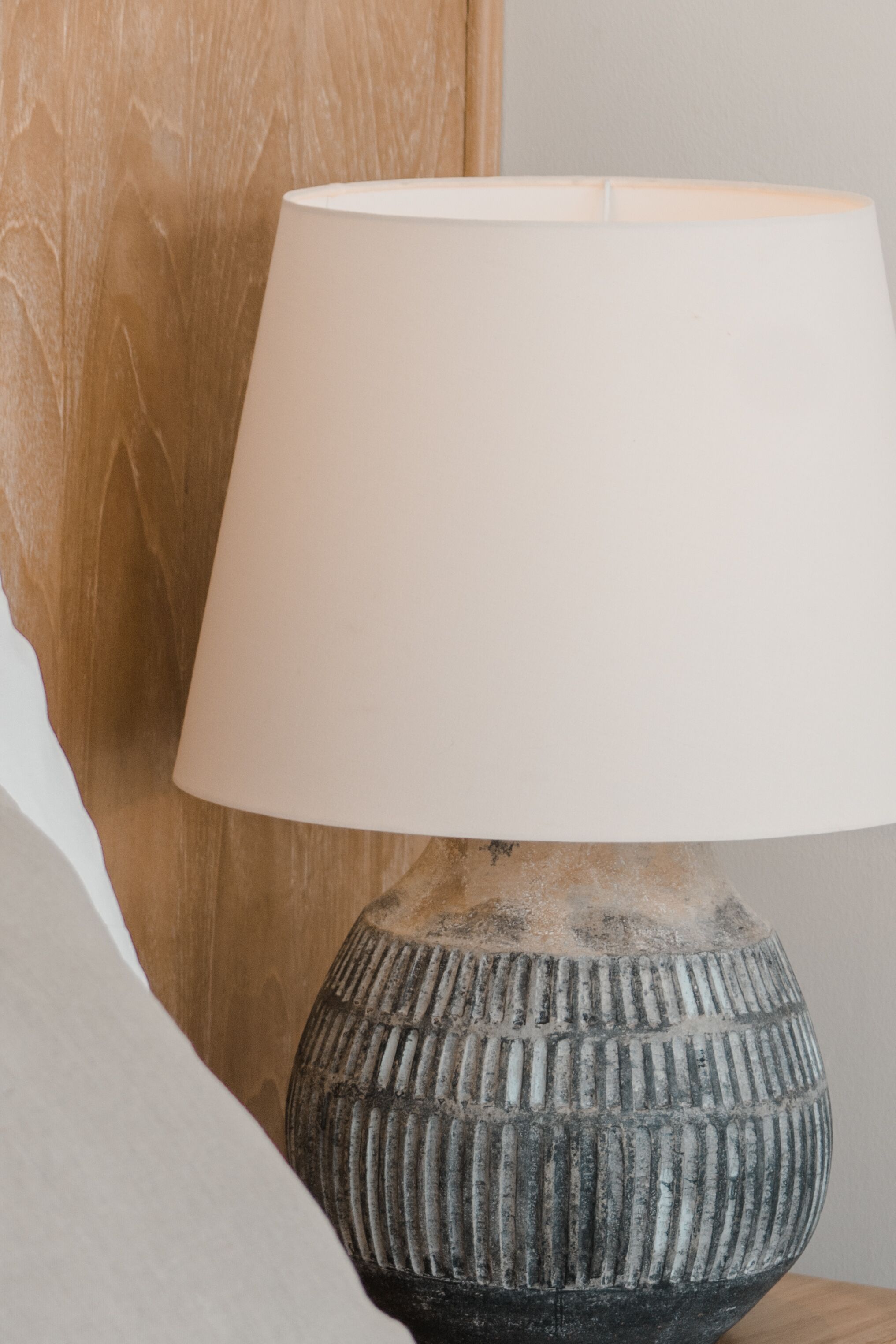 A lamp with a ribbed base and a white lampshade on a wooden surface.
