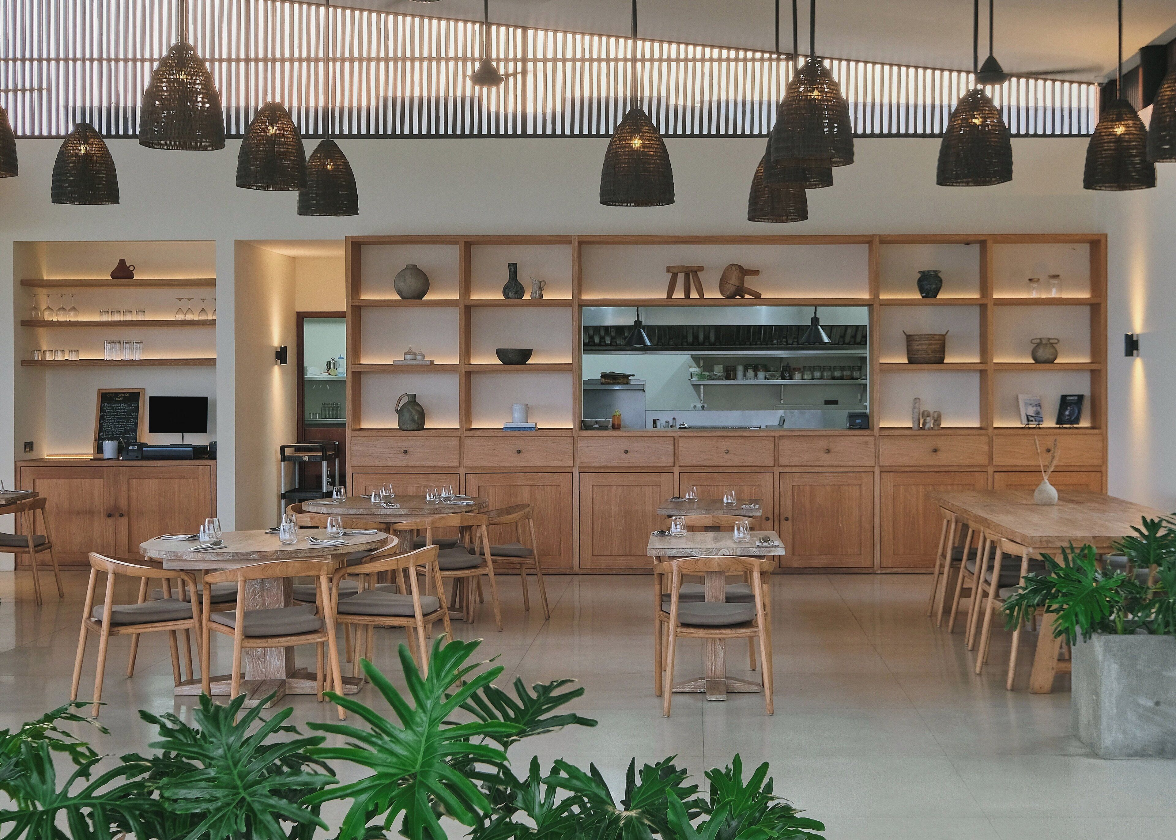 Un restaurante moderno con mobiliario de madera, iluminación colgante y varios objetos decorativos en estanterías.