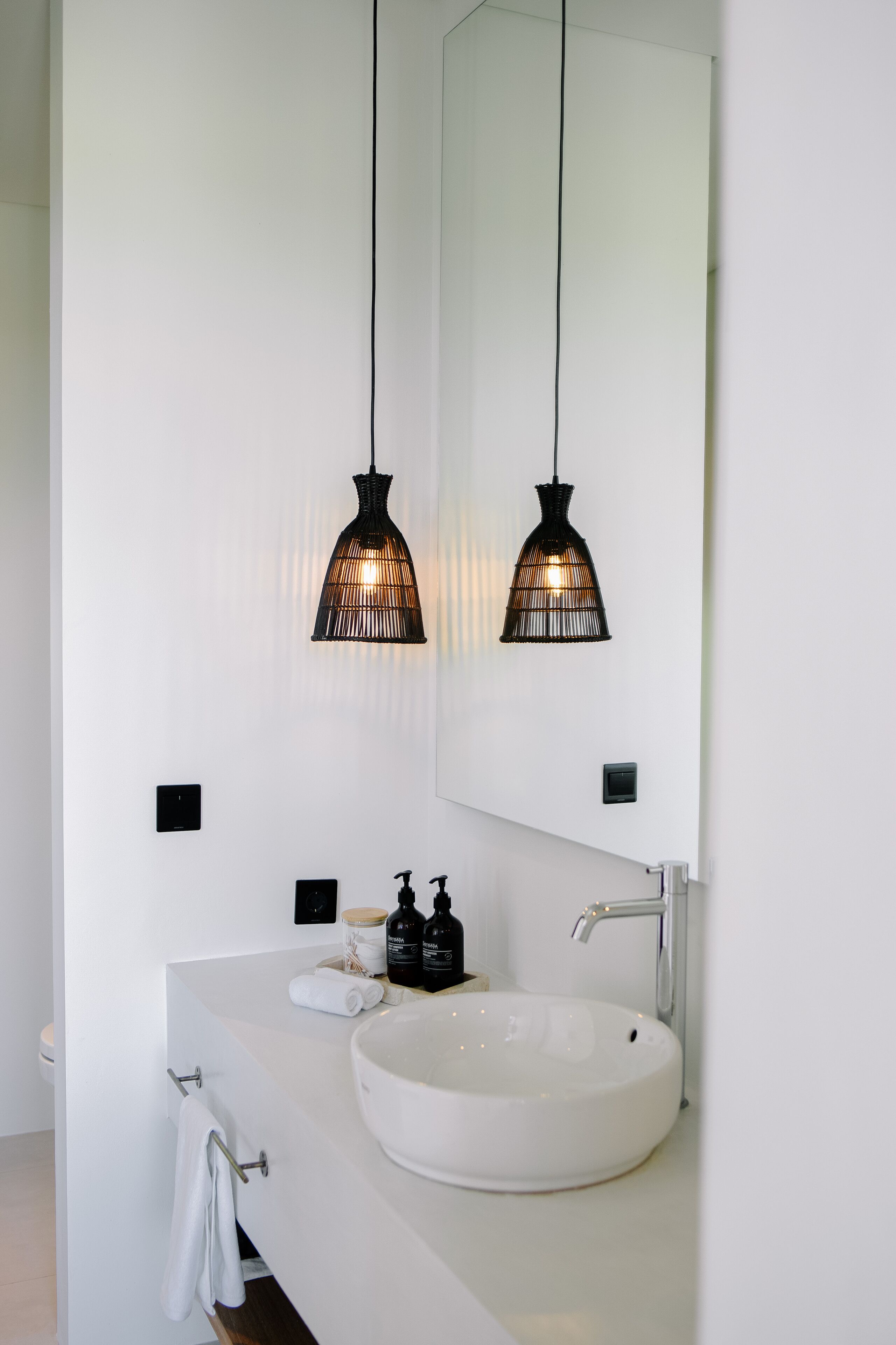 A modern bathroom with a white sink, black fixtures, and two hanging pendant lights.