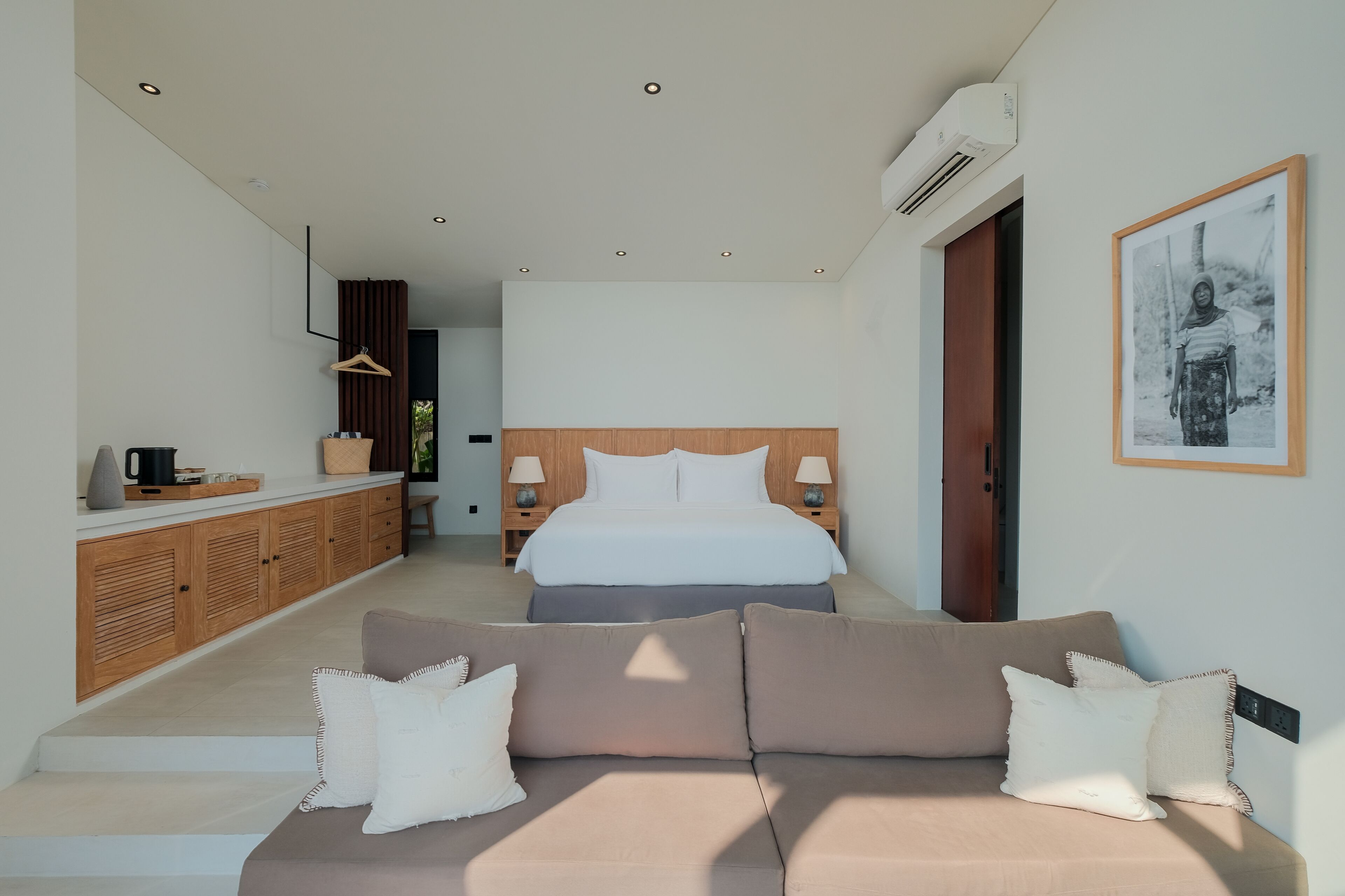 A modern hotel room with a large bed, a sofa, a wooden cabinet, and a framed picture on the wall.