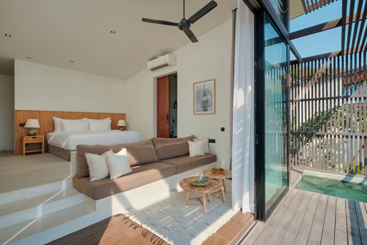 Ein modernes Schlafzimmer mit einem Bett, einem Sofa, einem kleinen Tisch und einem Balkon mit Blick.