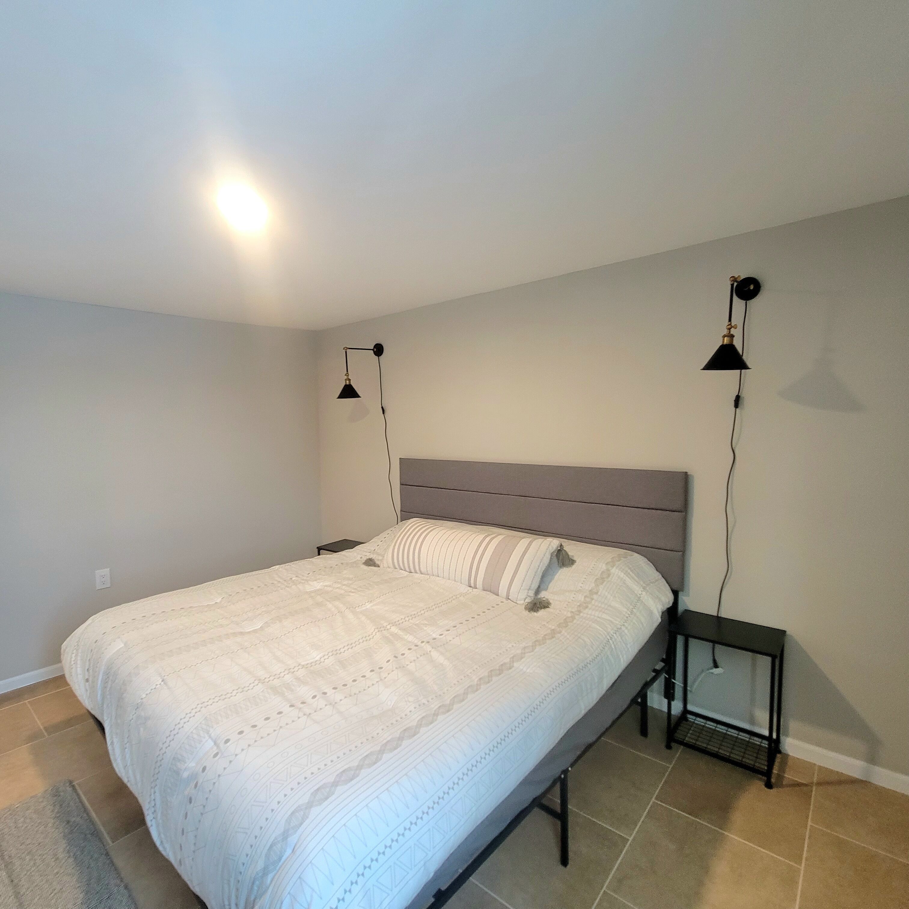 A bedroom with a bed, a nightstand, a wall-mounted lamp, and a floor lamp.