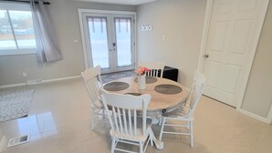 Un comedor con una mesa redonda, sillas blancas y un ventanal con cortinas.
