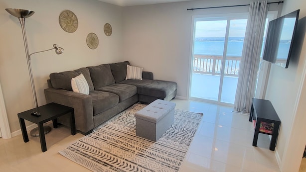 Un salón moderno con un sofá seccional gris, una mesa de centro negra, una alfombra estampada y un ventanal con vista al mar.