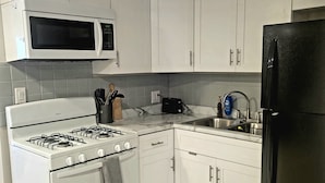 Una cocina con gabinetes blancos, una estufa a gas, un microondas, un refrigerador negro y un lavaplatos.