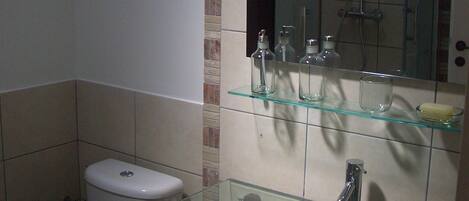 Un baño con lavamanos de vidrio, inodoro y ducha.