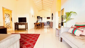 A spacious living area with a sofa, a TV, a dining table, and a kitchen in the background.