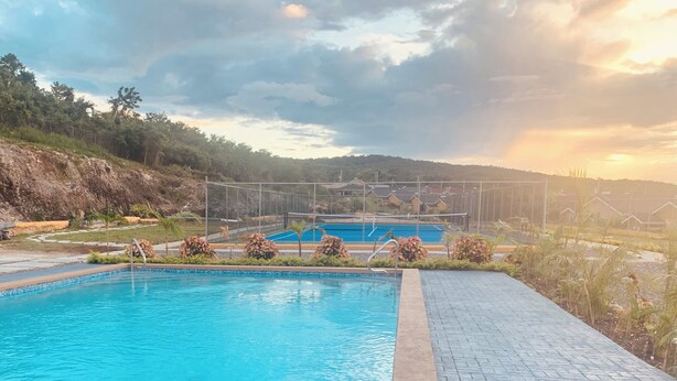 A swimming pool with a paved deck, surrounded by plants and a view of hills in the background.