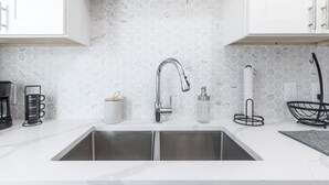 Een moderne keuken met een witte backsplash van hexagontegels, een roestvrijstalen spoelbak en een zwarte koffiezetapparaat.