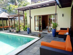 Ein Poolbereich mit überdachter Sitzgelegenheit, einem Pool und einem Gebäude mit großen Fenstern und Türen.
