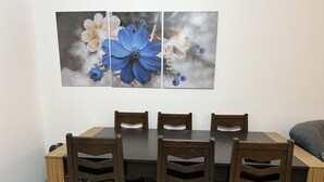 A dining area with a rectangular table, six wooden chairs, and a wall-mounted floral artwork. - Luxury apartment new cairo alrehab (Cairo Governorate)