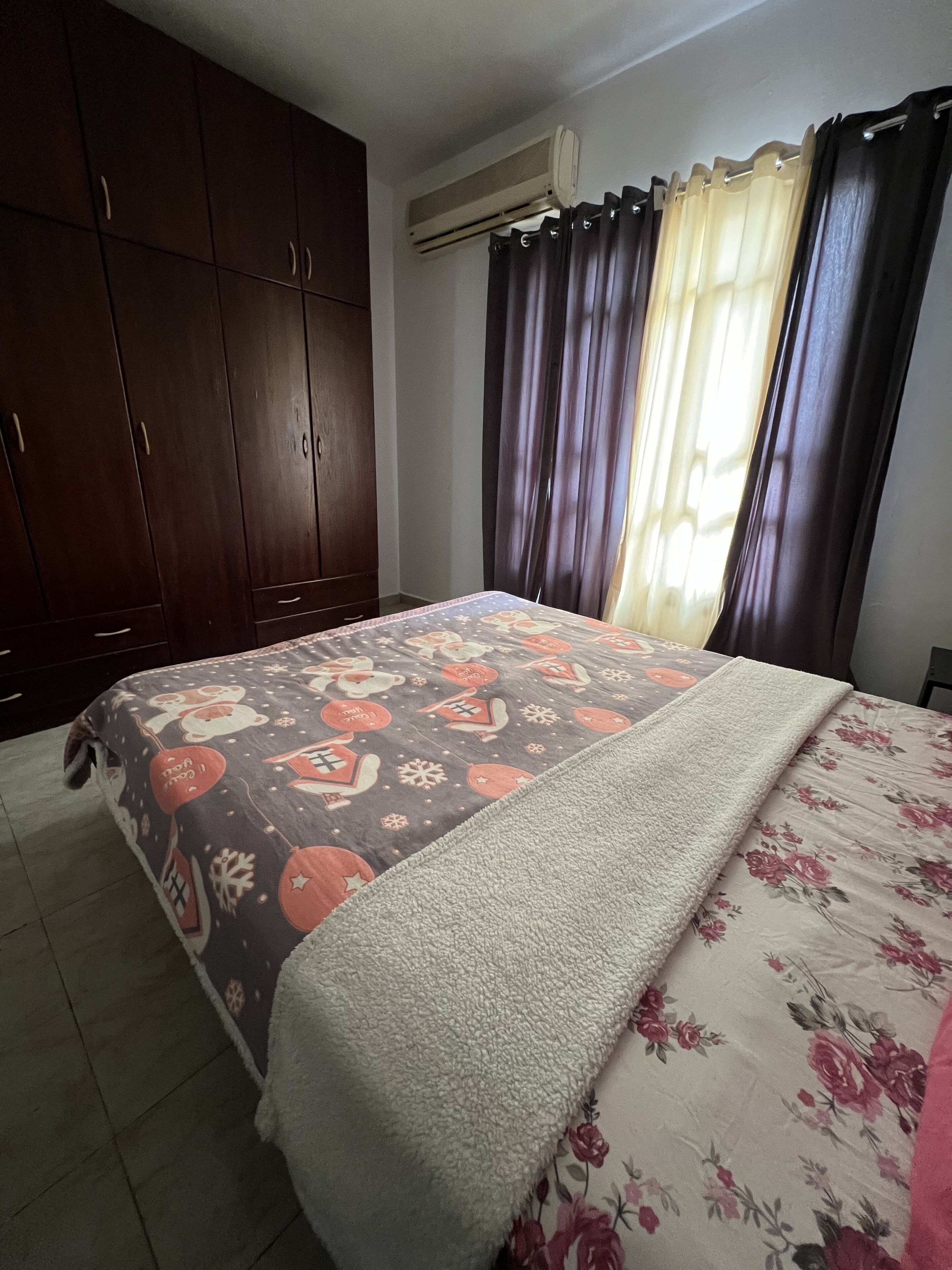 Une chambre à coucher comprenant un lit, une armoire, une fenêtre avec des rideaux et un appareil de climatisation.